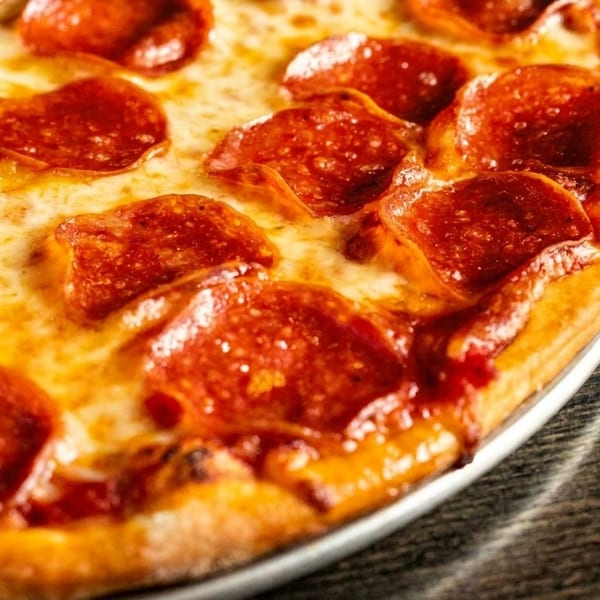 Close-up of a pepperoni pizza with melted cheese and a golden crust on a dark wooden table.