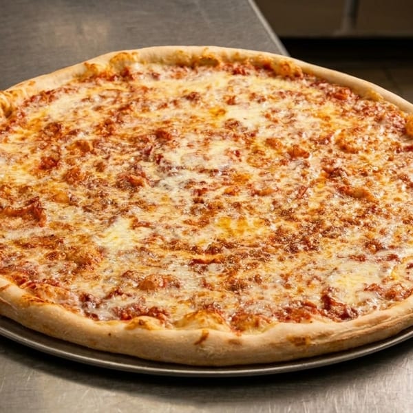 A large, freshly baked cheese pizza on a metal pan, next to a stack of paper plates.